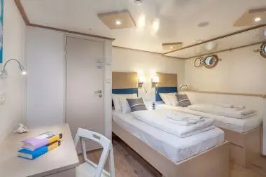 Premium Superior twin cabin on the MV Majestic featuring porthole windows, modern lighting, and sleek decor designed for guests on the 2026 Southern European Naturist Nude Cruise through coastal destinations.