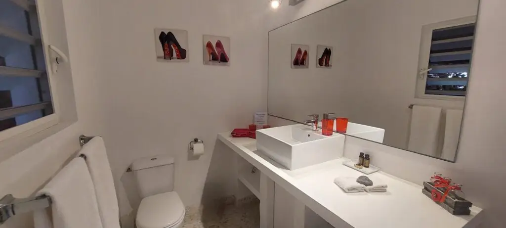 Elegant white bathroom with red accents, mirror, and modern sink at Studio Red Passion, Caribbean nude clothing optional resort