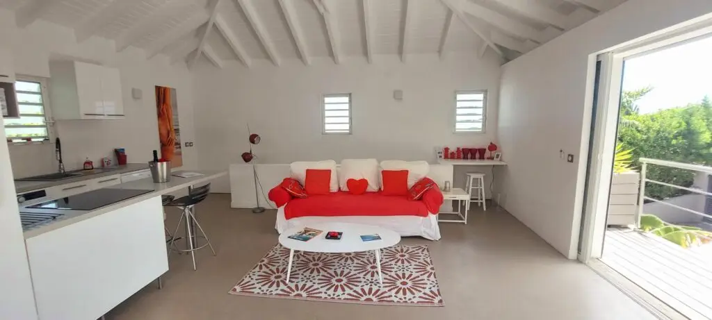 Modern living room with red sofa, open kitchen, and tropical light streaming in at Studio Red Passion, Caribbean adult-only resort suite