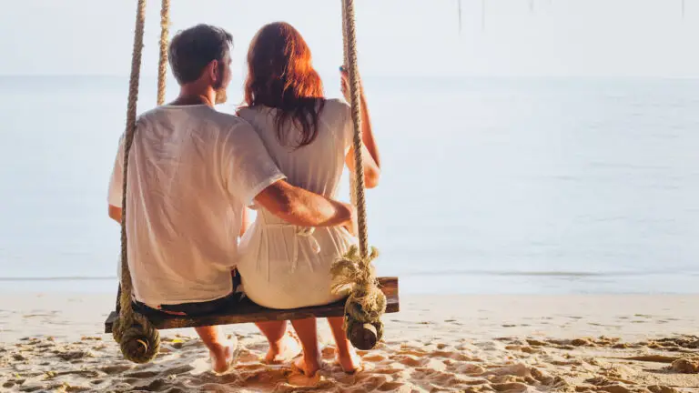 Couple sitting on a beach swing at sunset sharing a quiet romantic moment while exploring the swinging lifestyle together
