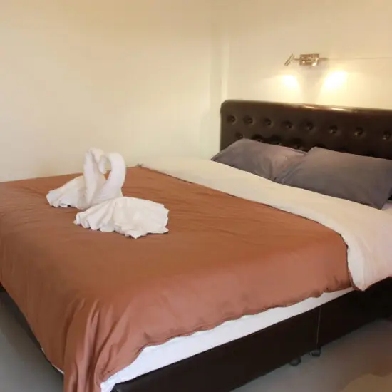Bright bedroom with king bed and towel swan decoration at Barefeet Naturist Resort in Bangkok
