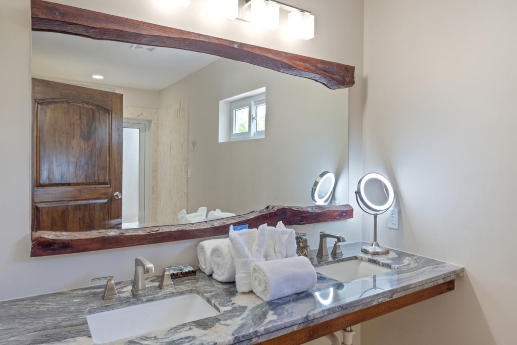 Modern spa style bathroom with double vanity, stone countertops, and custom wood mirror in the Stingray Bungalow during the Nude Takeover 2026 in Belize