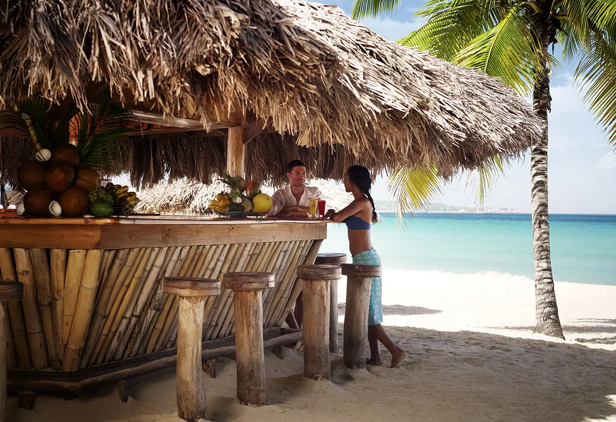 Couple enjoying drinks at Couples Negril beach bar in Jamaica, adults only all inclusive resort for honeymoon and anniversary travel