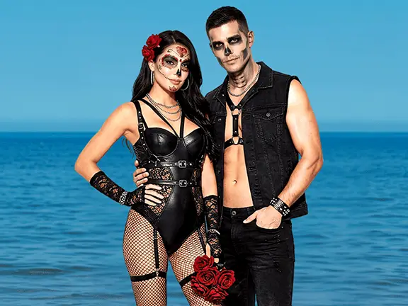 Couple in dramatic Sugar Skull inspired costumes and Day of the Dead makeup during Bliss Cruise swinger travel fiesta theme night on the beach
